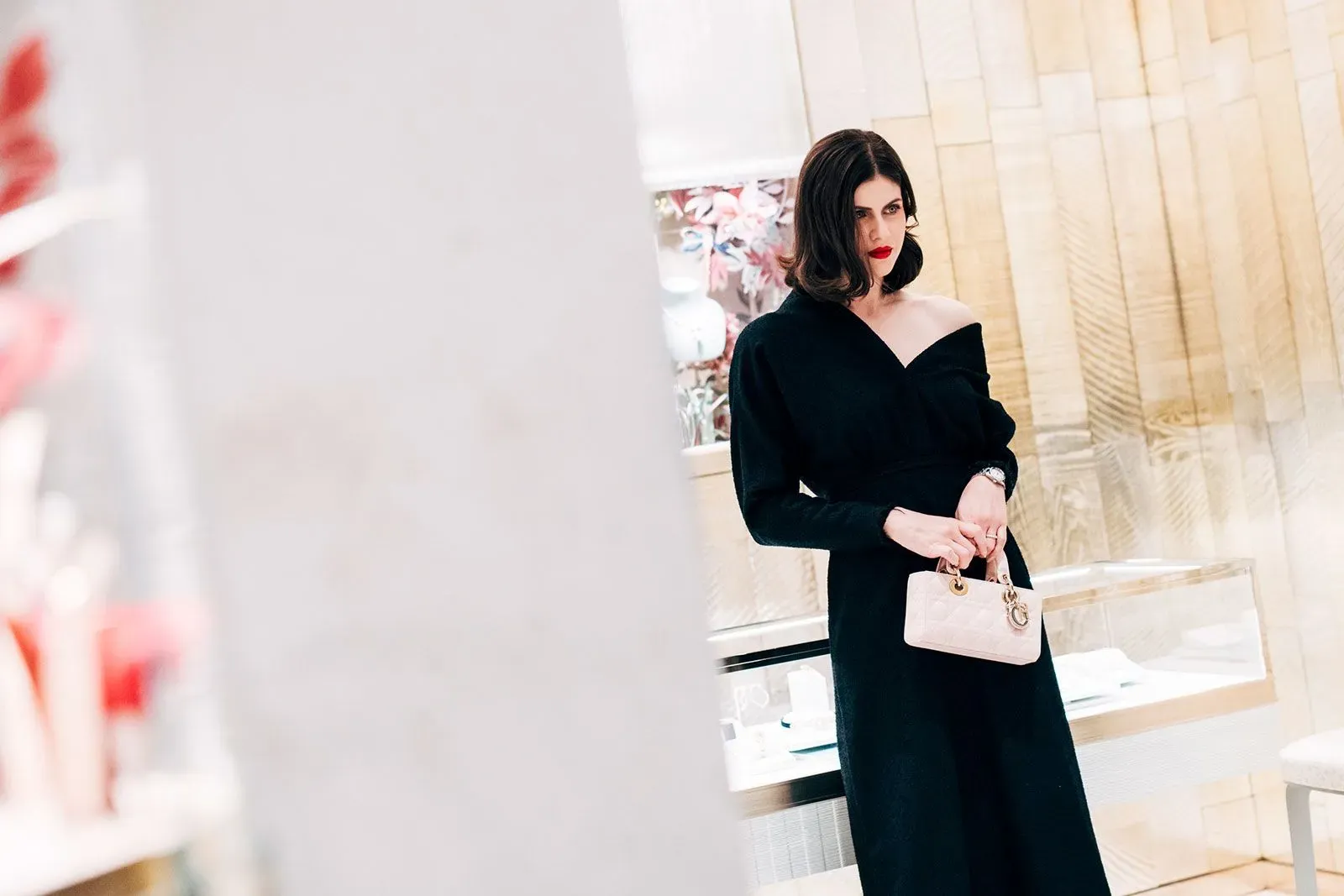 امرأة ترتدي فستاناً أسود أنيقاً وتحمل حقيبة صغيرة، تظهر في متجر فاخر، تعكس أجواء أسبوع الموضة في نيويورك.