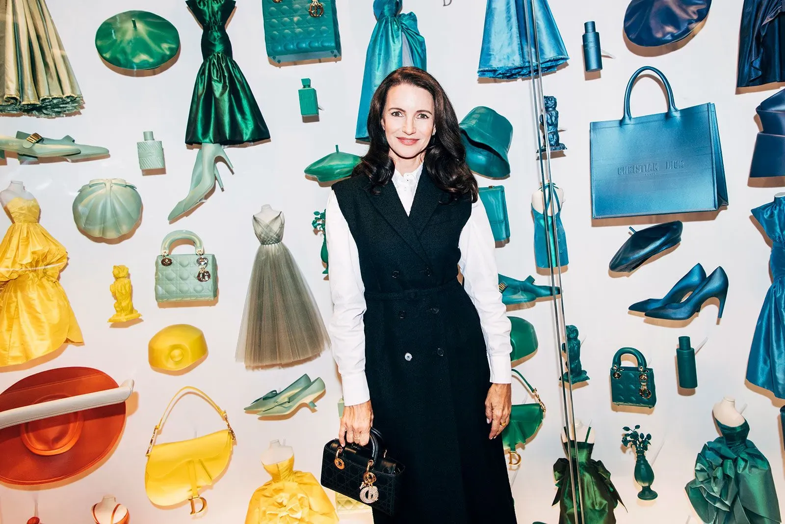 امرأة ترتدي سترة سوداء وقميص أبيض، تقف أمام جدار مزين بمجموعة متنوعة من الملابس والإكسسوارات الملونة، في حدث متعلق بالأزياء.