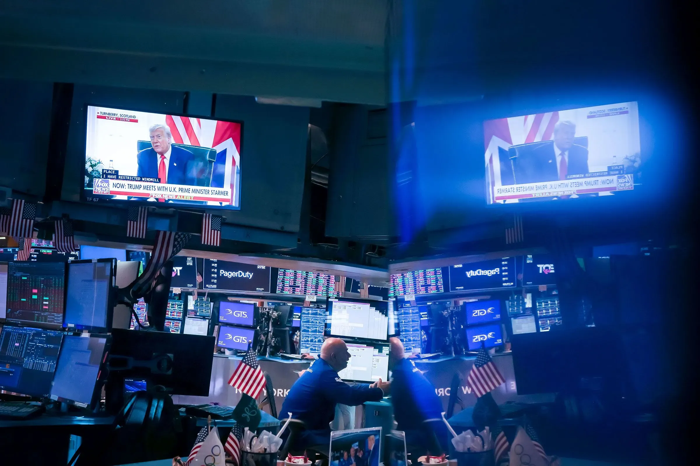 لقطة من قاعة تداول الأسهم تُظهر شاشات تعرض تصريحات الرئيس ترامب، مع وجود متداولين يعملون في الخلفية.