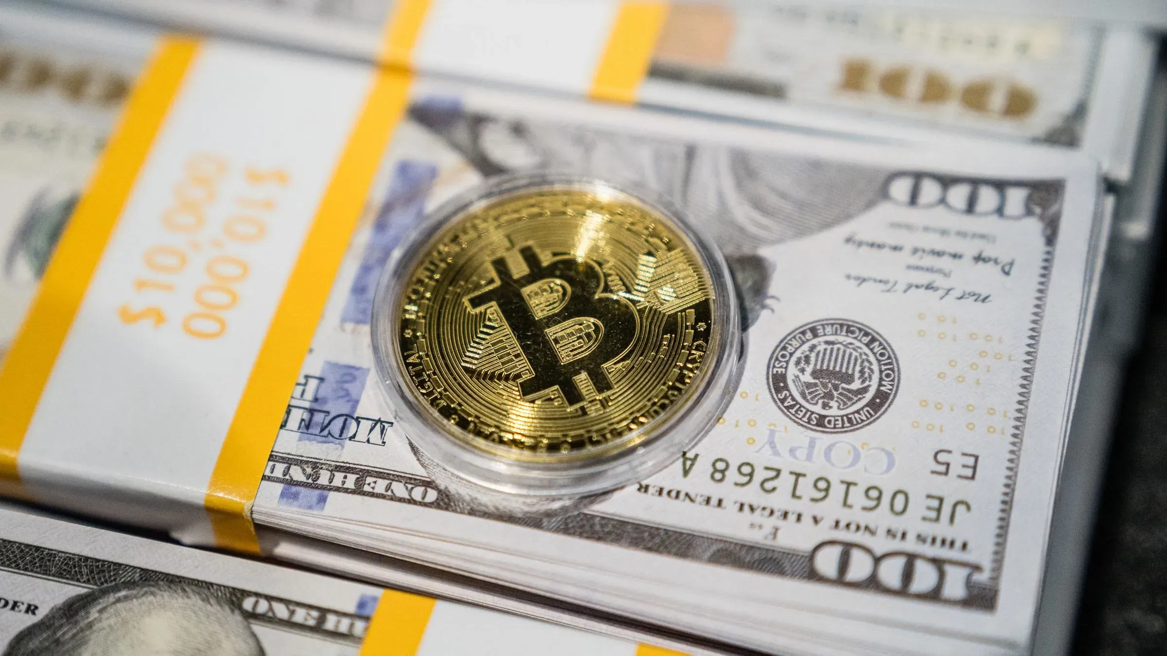 عملة بيتكوين الذهبية موضوعة على حزمة من الدولارات الأمريكية، تعكس النقاش حول تنظيم العملات الرقمية في الولايات المتحدة.