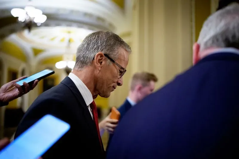 رجل يرتدي بدلة رسمية، يبدو أنه يتحدث مع مجموعة من الأشخاص في ممر مجلس الشيوخ، مع التركيز على النقاشات حول ميزانية الحكومة.