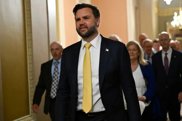 نائب الرئيس جيه دي فانس يتقدم في ممر مجلس الشيوخ بعد التصويت على مشروع قانون ترامب، مع وجود أعضاء آخرين في الخلفية.