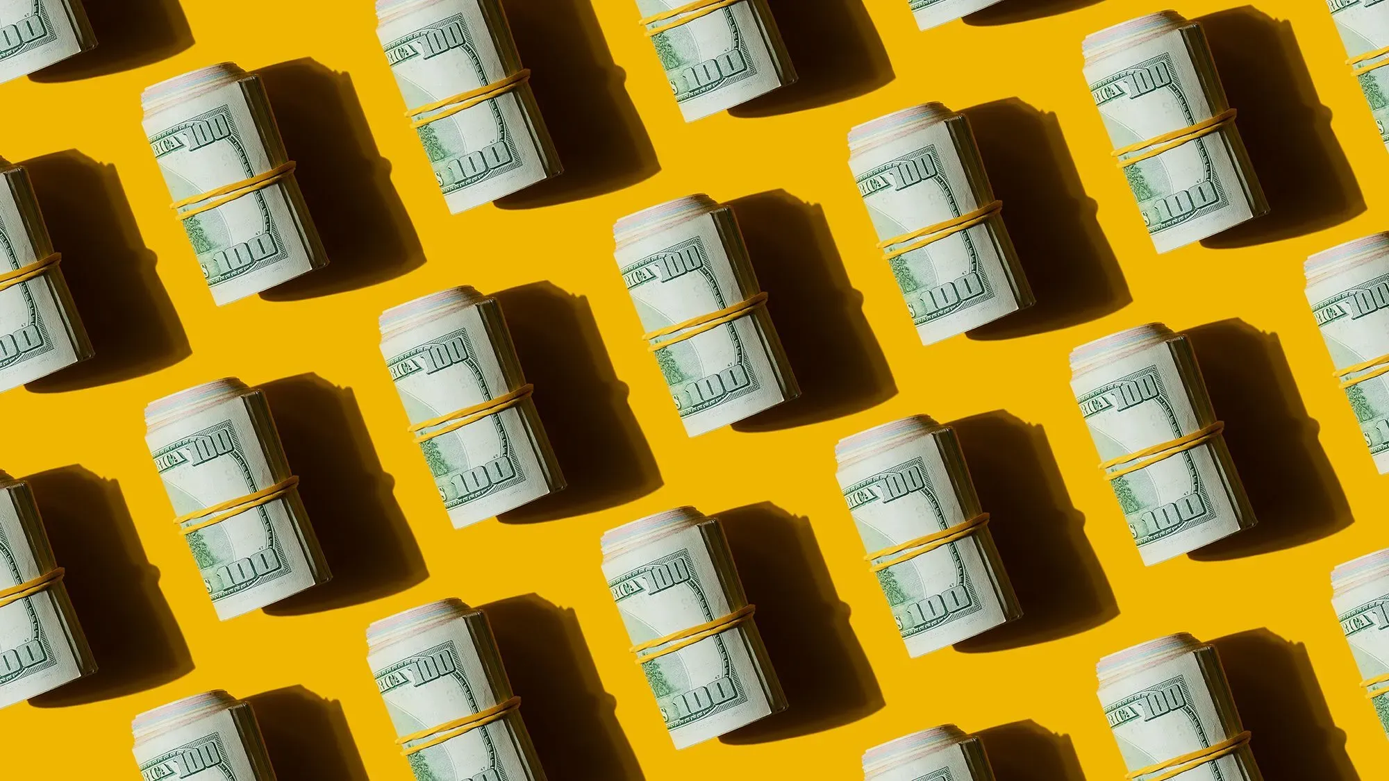أكوام من الدولارات الملفوفة بشريط مطاطي على خلفية صفراء، تمثل استراتيجيات الادخار والتخطيط المالي للتقاعد.