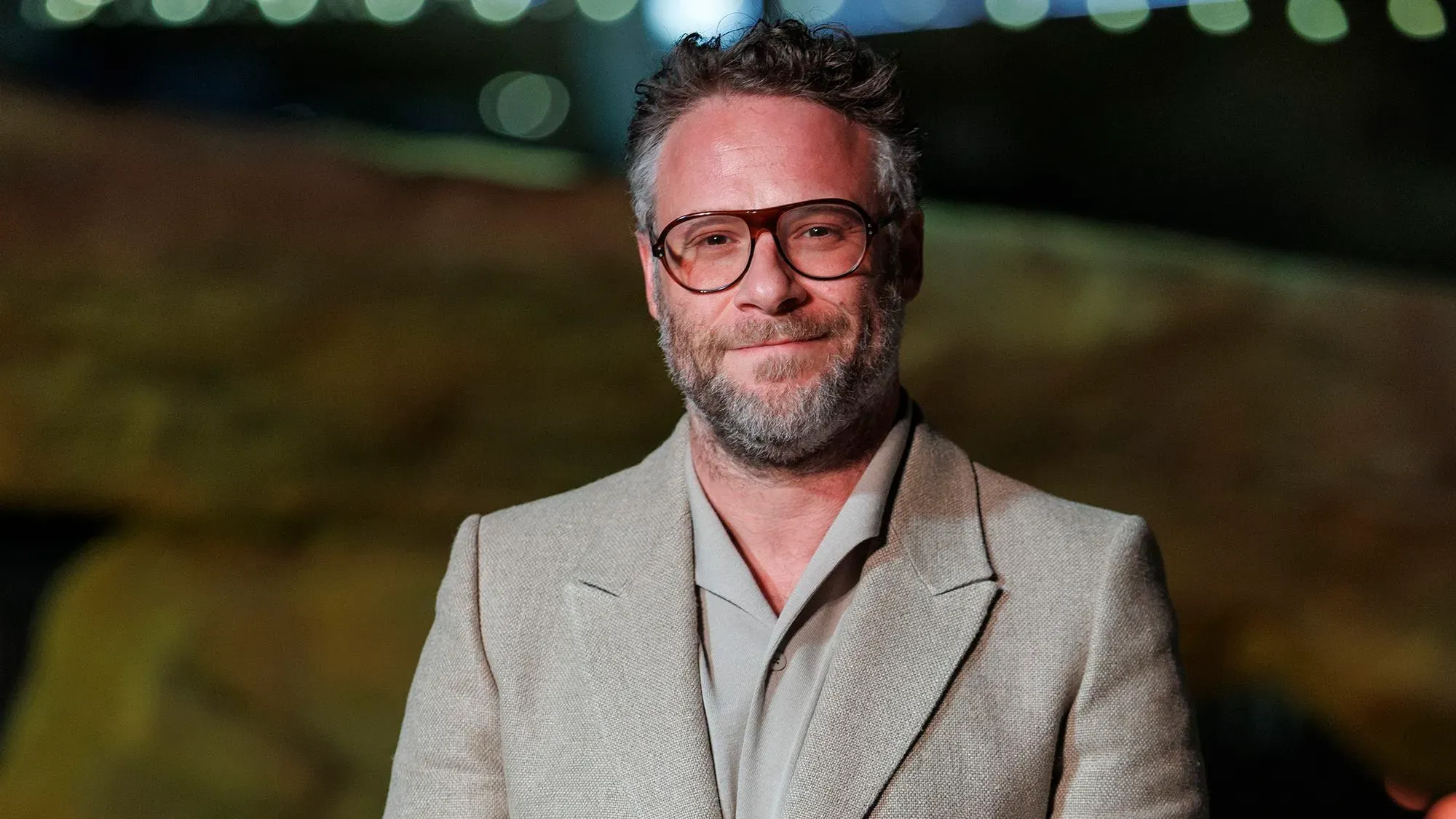 سيث روجن مبتسم في حدث رسمي، يرتدي بدلة أنيقة، مع خلفية غير واضحة، مما يعكس شخصيته كمدير تنفيذي في فيلم "الاستوديو".