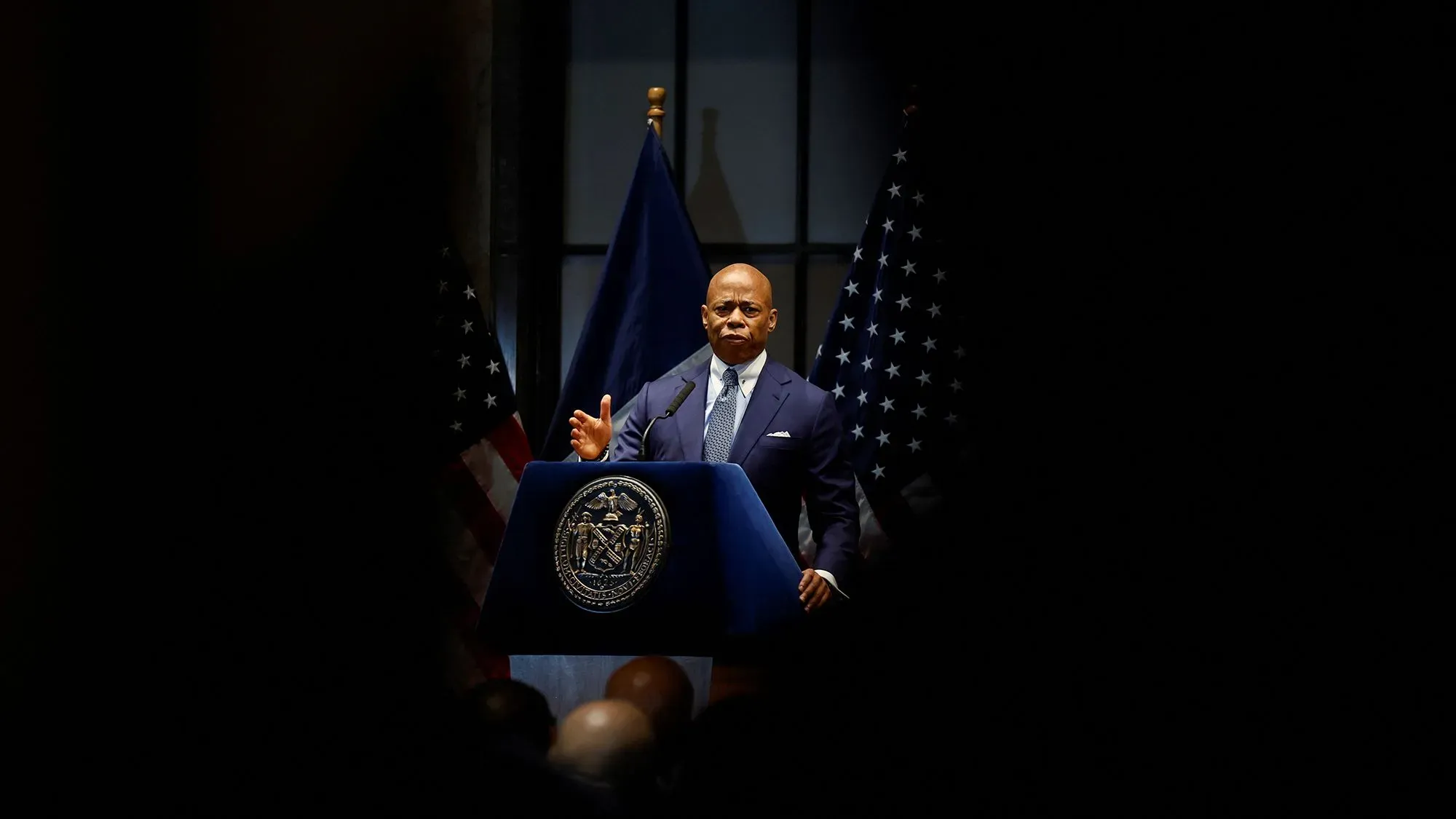 خطاب عمدة مدينة نيويورك إريك آدامز خلال مؤتمر صحفي، مع علمين أمريكيين خلفه، وسط أجواء مشحونة بالتوترات القانونية.