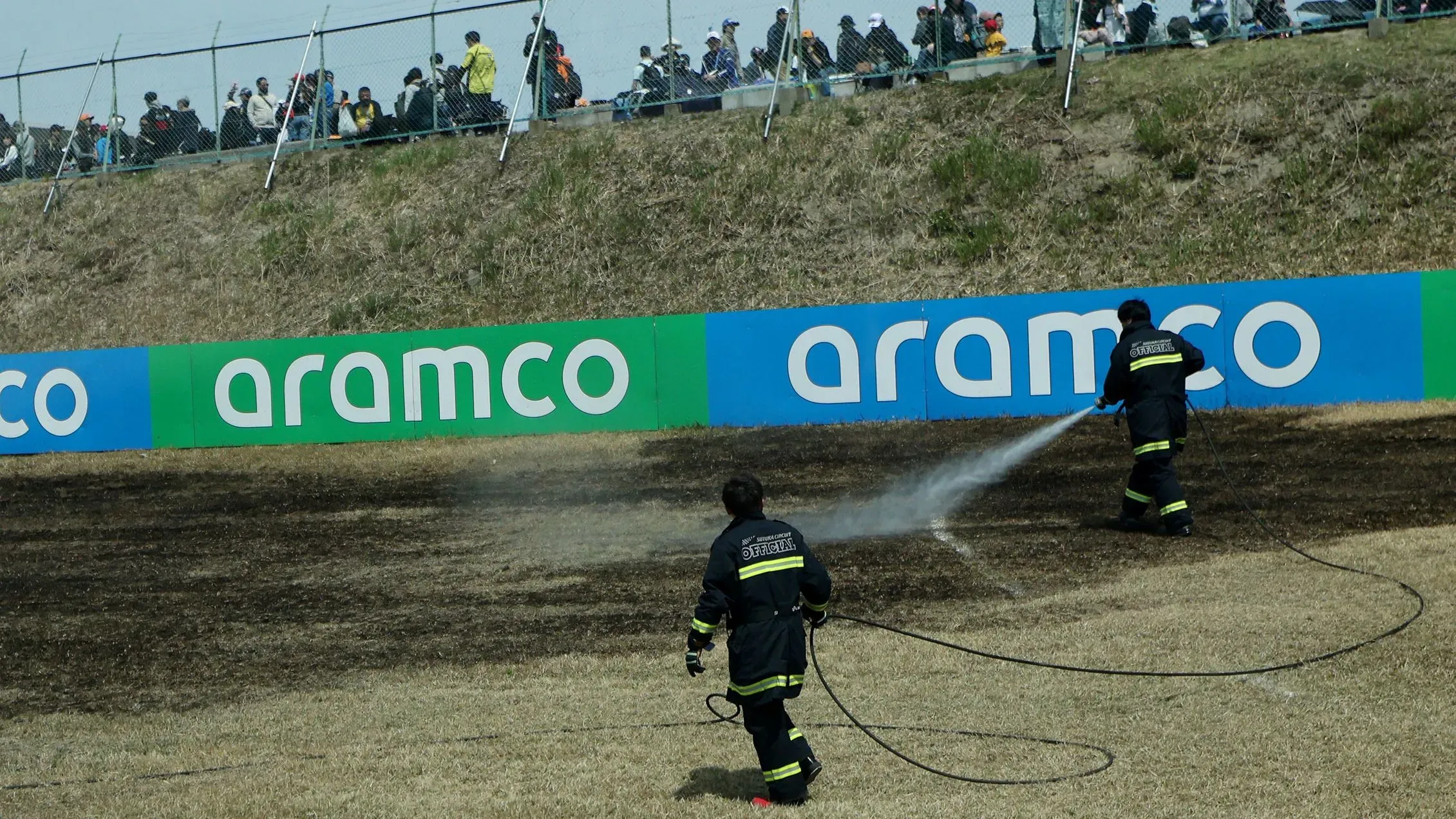 رجال الإطفاء يقومون برش المياه على العشب المحترق في حلبة سوزوكا خلال سباق جائزة اليابان الكبرى، وسط جمهور المتفرجين.