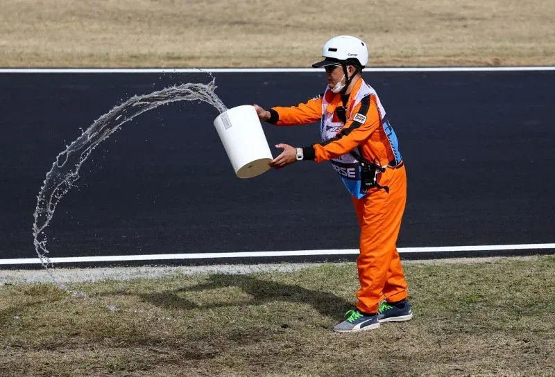 شخص يرتدي زيًا برتقاليًا يقوم بسكب الماء على العشب الجاف بجانب مضمار سباق جائزة اليابان الكبرى، في محاولة للحد من حرائق الأعشاب.