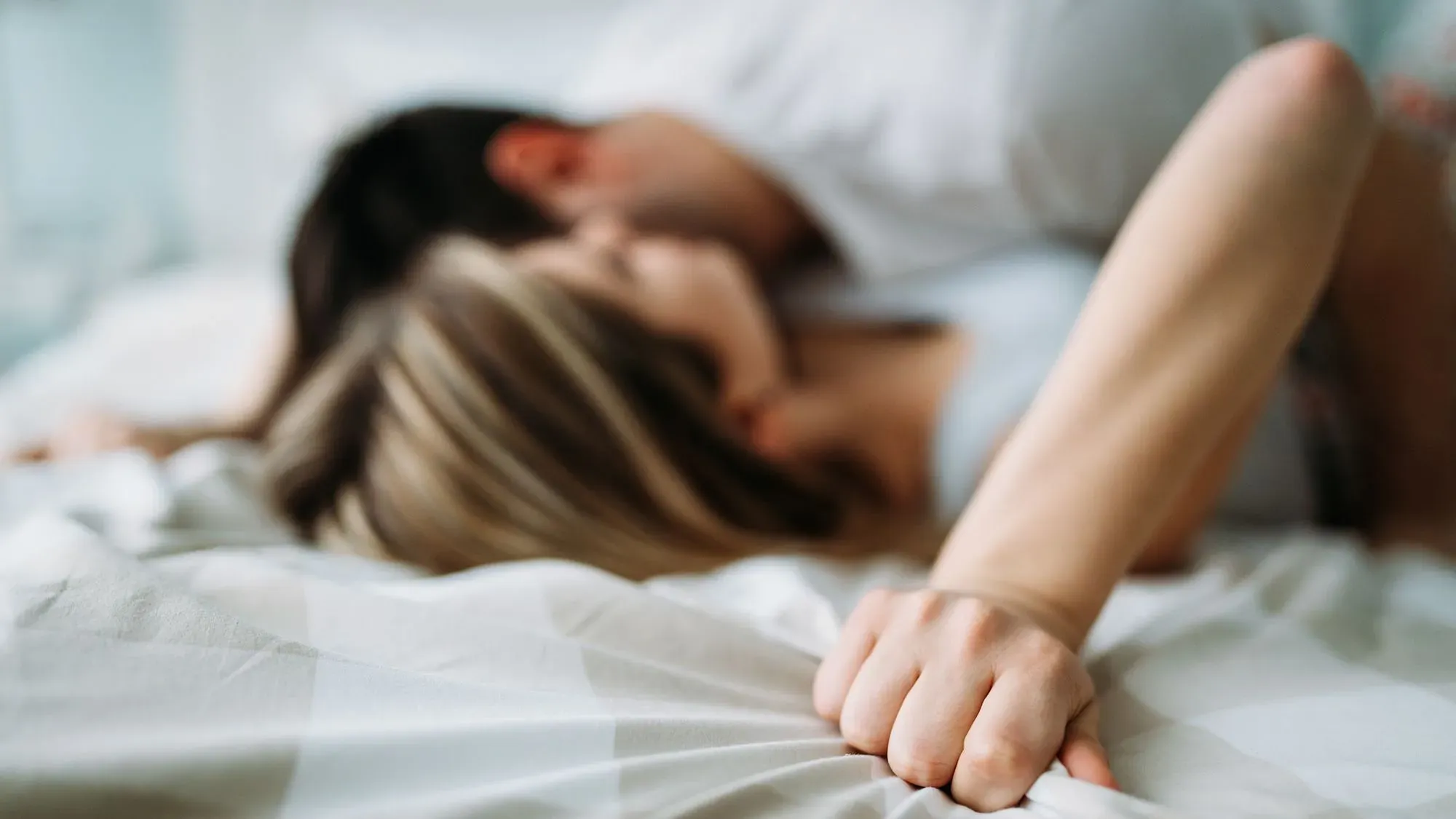 زوجان يتعانقان على السرير، يعكسان تجربة الجماع المؤلم التي تعاني منها العديد من النساء، كما يُشير المقال إلى أهمية الدعم والعلاج.