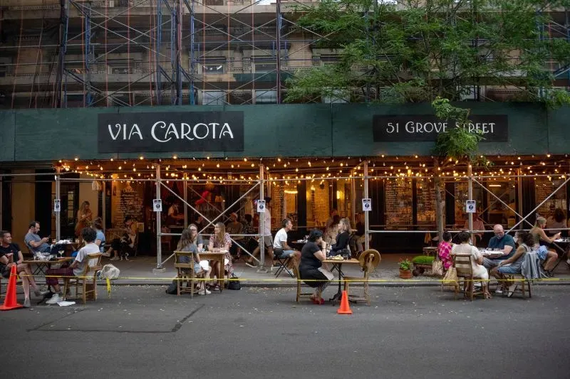 مطعم "فيّا كاروتا" في نيويورك يقدم تجربة تناول طعام في الهواء الطلق مع أضواء متلألئة وطاولات على الرصيف، وسط أجواء حيوية.