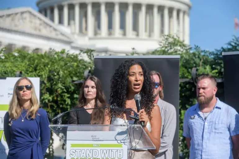 ناجية تتحدث أمام مبنى الكابيتول الأمريكي خلال تجمع للمطالبة بالشفافية في قضية جيفري إبشتاين، مع حضور داعمين خلفها.