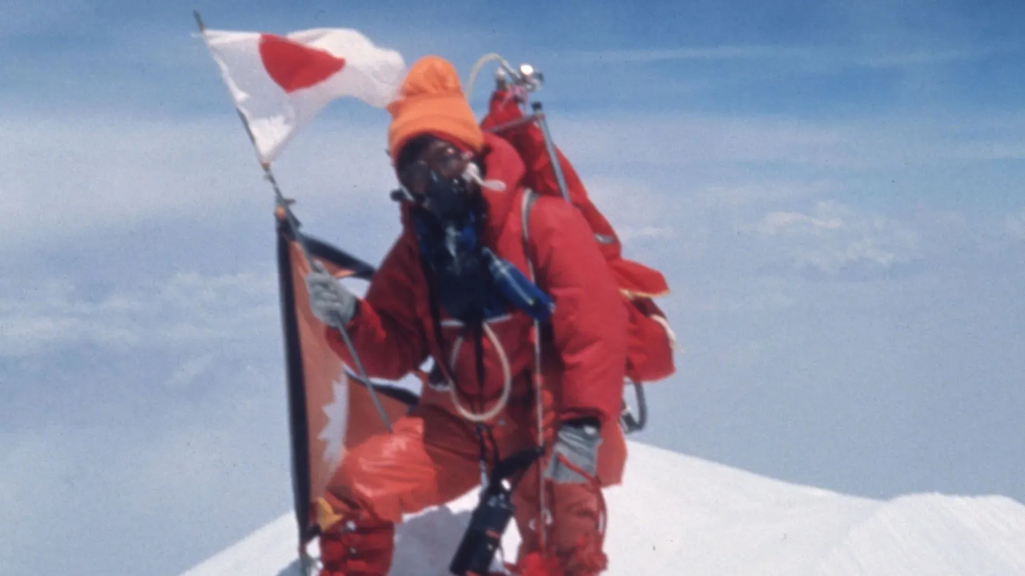 جونكو تاباي، أول امرأة تتسلق إيفرست، تحمل العلم الياباني على القمة في 16 مايو 1975، وسط سماء زرقاء.