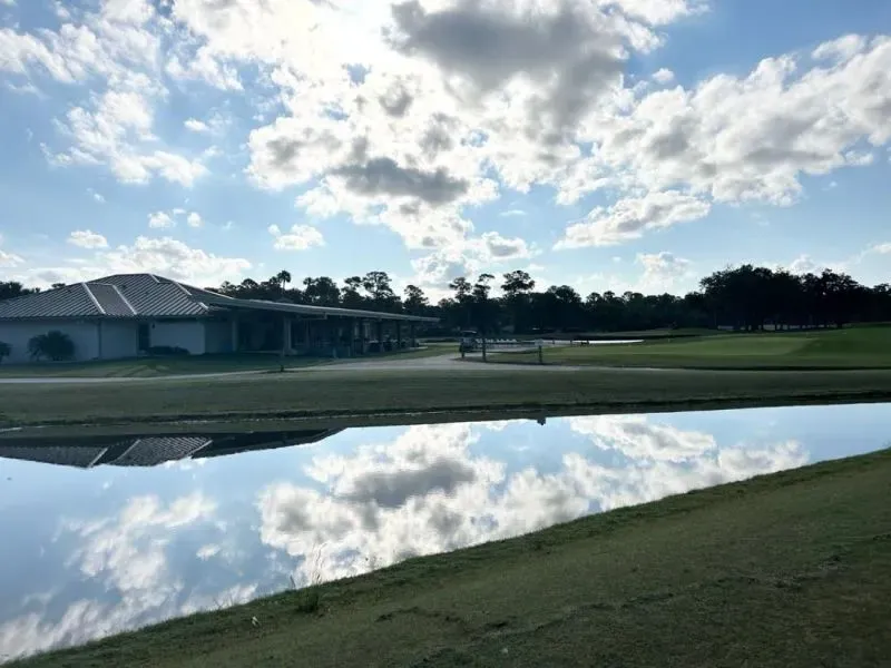 منظر لمرافق نادي ساوجراس بلايرز مع ملعب جولف ومسطحات مائية تعكس السماء الزرقاء والغيوم، مما يبرز جمال المجتمع المحيط.