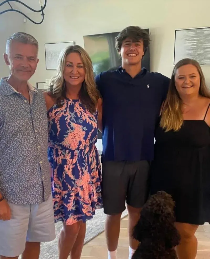 عائلة بورشيل تتوسط الصورة، حيث يقف الأب والأم مع ابنيهما، بينما يظهر كلب أسود بجانبهم في منزل حديث.