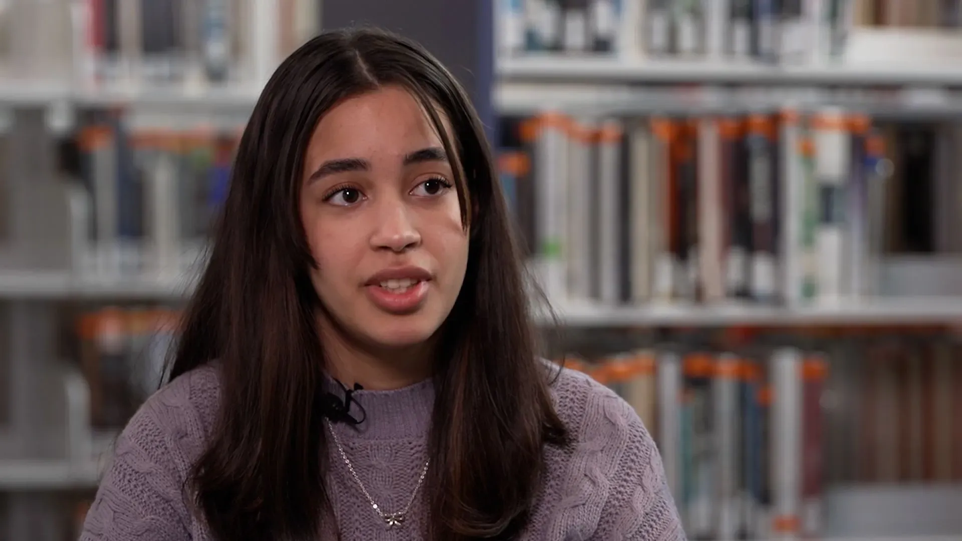 أليشا أورتيز، 19 عامًا، تتحدث عن تحدياتها في التعليم والأمية، مع خلفية من الكتب في المكتبة.