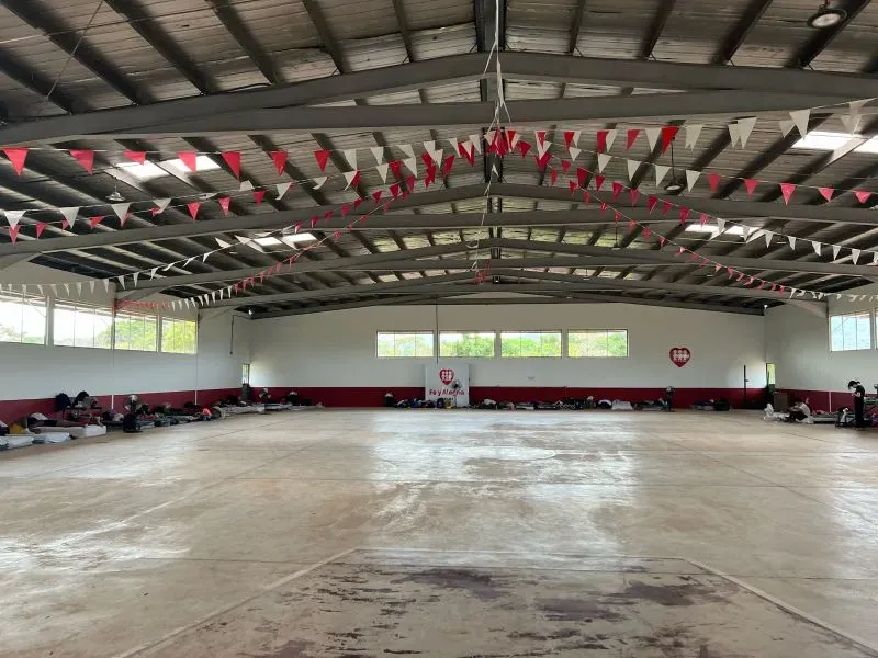 مساحة كبيرة في مأوى للمهاجرين في بنما، تحتوي على فرشات مرتبة على الأرض وزينة علمية، تعكس ظروف الإقامة الصعبة.