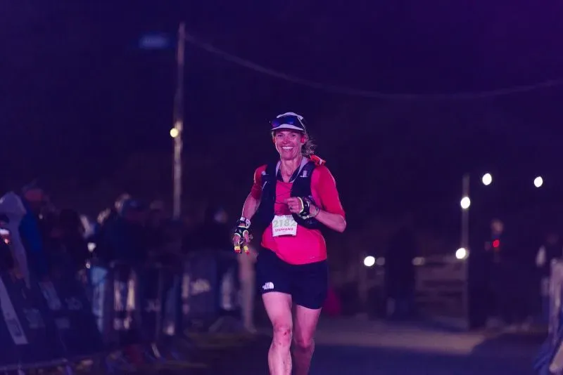 ستيفاني كيس تجري في سباق ألترا تريل سنودونيا، مبتسمة وتظهر عزمها، رغم التحديات كأم، وسط أضواء السباق وجمهور متحمس.