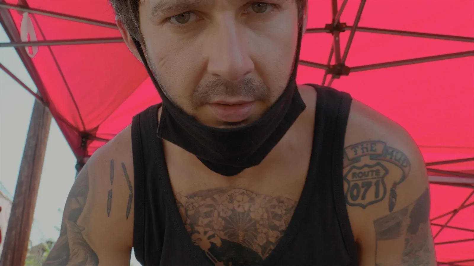 شيا لابوف يظهر في مشهد من الفيلم الوثائقي "Slauson Rec"، مرتديًا قناعًا، مع خلفية حمراء، يعكس تفاعلاته مع طلابه في فرقة المسرح.