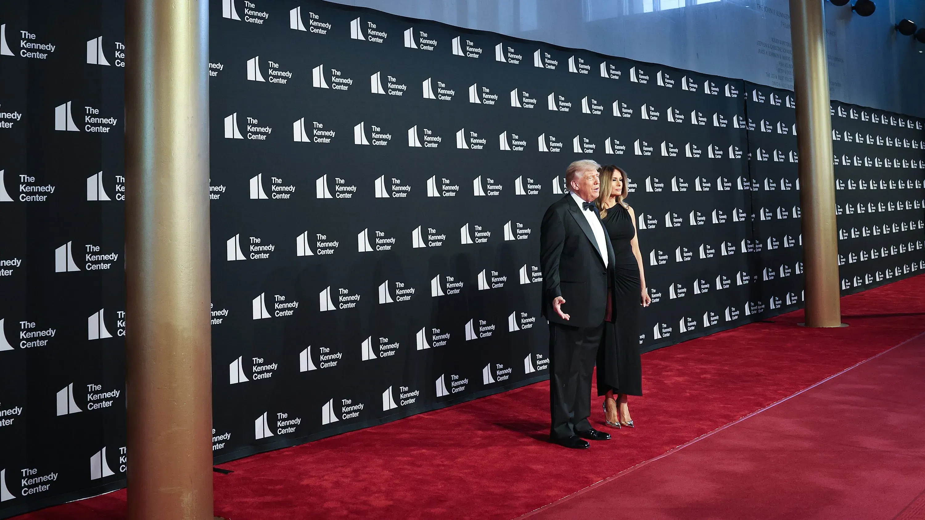 دونالد ترامب وميلانيا ترامب يقفان على السجادة الحمراء في مركز كينيدي، مع خلفية تحمل شعار المركز، خلال حدث ثقافي مثير للجدل.