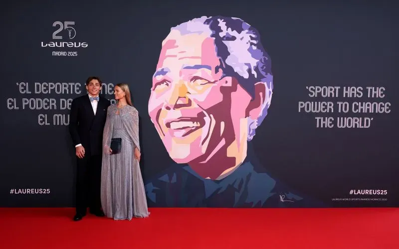 حضور شخصين يرتديان ملابس أنيقة أمام جدارية تصور نيلسون مانديلا، مع عبارة "للرياضة القدرة على تغيير العالم" في احتفال جوائز لوريوس الـ25.
