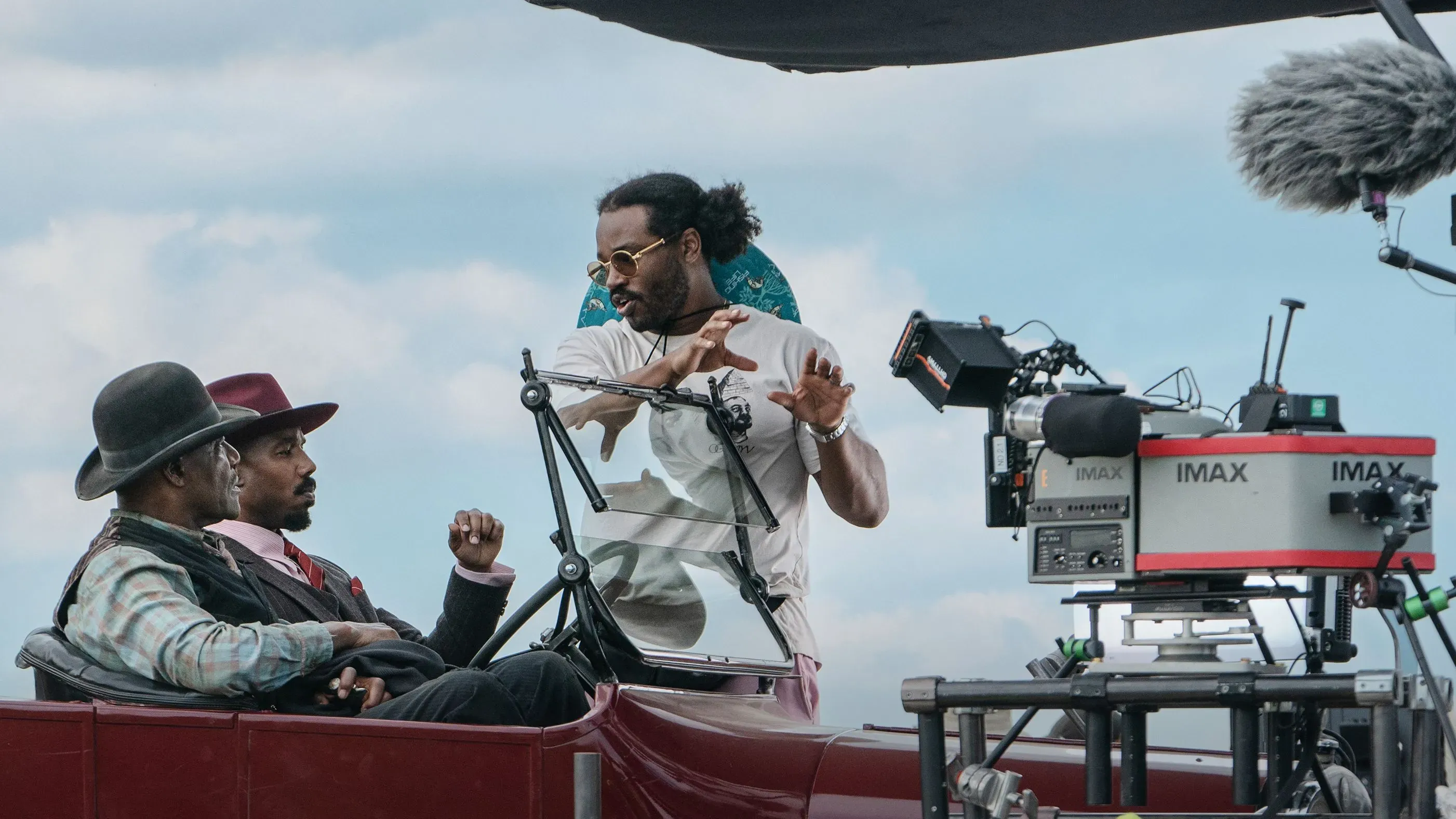 مشهد من تصوير فيلم "المذنبون" حيث يتفاعل المخرج مع الممثلين في سيارة، مع معدات تصوير IMAX في الخلفية.