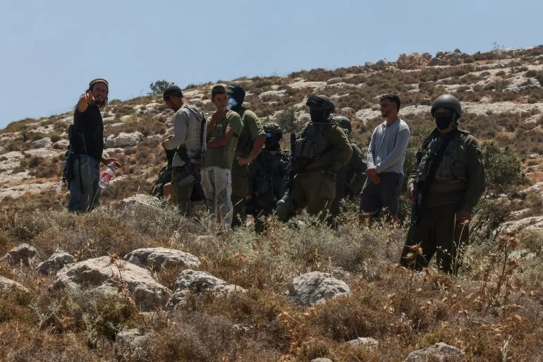 مجموعة من الجنود الإسرائيليين والمستوطنين في منطقة جبلية بالضفة الغربية، تعكس التوترات المستمرة بين المستوطنين والفلسطينيين.