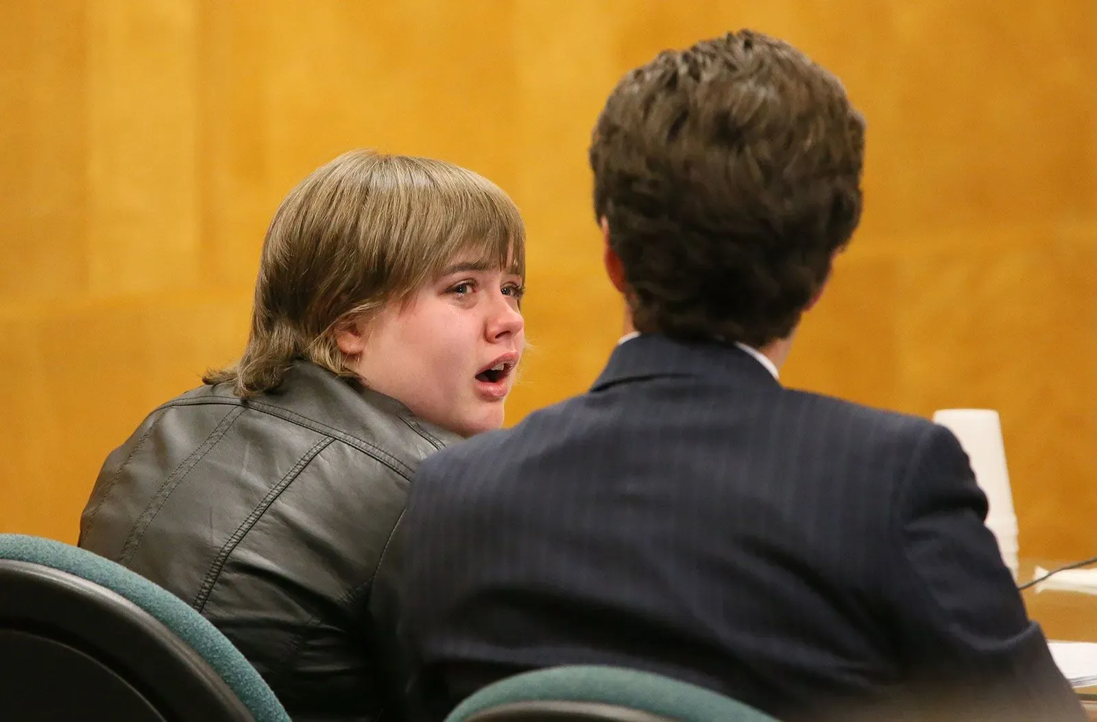 امرأة تبكي أثناء جلسة محكمة، تجلس بجوار محاميها، في سياق قضية طعن زميلة لها في مدرسة ابتدائية.