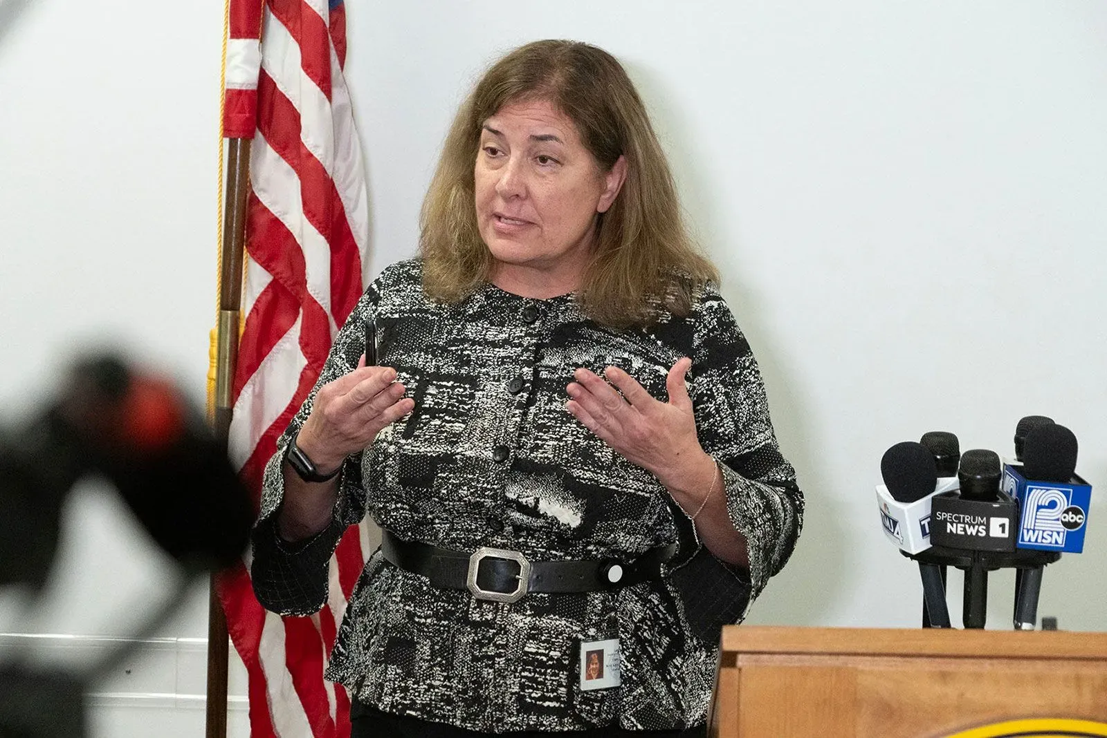 امرأة تتحدث في مؤتمر صحفي، مع وجود علم أمريكي خلفها، تتناول قضية هروب مورغان غايسر بعد الحكم عليها.