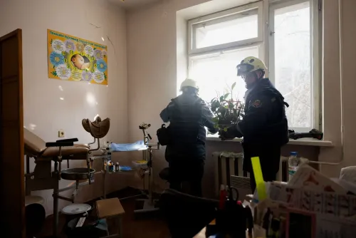 رجال إنقاذ يحملون نباتات من غرفة في مستشفى للولادة بعد الهجوم، مع وجود ملصق تعليمي على الحائط.