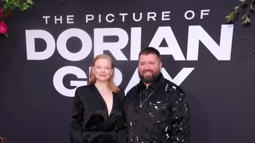 زوجان يقفان معًا أمام لافتة كبيرة تحمل عنوان "صورة دوريان غراي"، حيث يرتديان ملابس أنيقة تعكس أجواء المسرح.