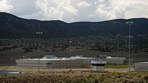 سجن ولاية إيلي في نيفادا، يظهر المبنى الرئيسي محاطًا بالجبال والسماء الملبدة بالغيوم، مع وجود أضواء عالية.