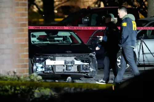سيارة سوداء متضررة في موقع حادث إطلاق نار، مع وجود ضباط من مكتب التحقيقات الفيدرالي في الخلفية، وسط شريط "لا تعبر" حول مكان الحادث.