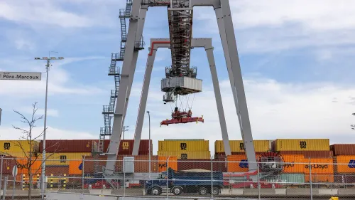 رافعة حاويات في ميناء، تحمل حاوية فوق شاحنات، مع خلفية من حاويات ملونة، تعكس أنشطة التجارة الدولية والرسوم الجمركية.