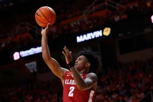 لاعب كرة سلة من فريق ألاباما يقوم بإطلاق الكرة نحو السلة، وسط أجواء حماسية في الملعب.