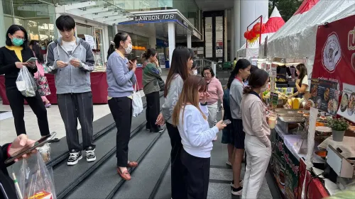 سكان بانكوك يرتدون سترات دافئة في سوق سيلوم، وسط أجواء باردة غير معتادة، مع بائعي الطعام في الخلفية.