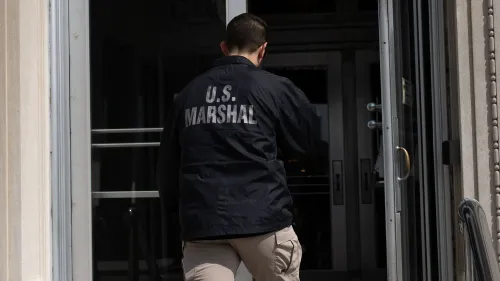 موظف من دائرة المارشال الأمريكية يرتدي سترة تحمل عبارة "U.S. MARSHAL" وهو يدخل مبنى، في سياق تعزيز الأمن للقضاة الفيدراليين.