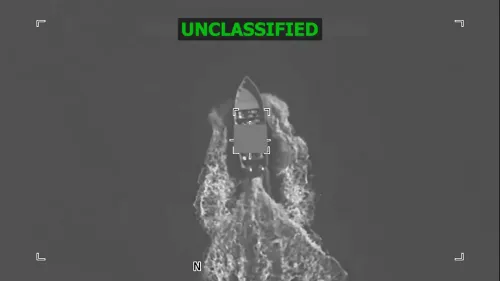 زورق صغير يبحر في البحر، يظهر من منظور جوي مع تفاصيل واضحة عن حركة المياه حوله، مما يعكس النشاط البحري.