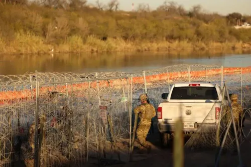 جنود يرتدون زيًا عسكريًا يعملون على الحدود الأمريكية مع وجود سياج من الأسلاك الشائكة وخلفهم سيارة بيك أب، مما يعكس التصعيد في جهود مراقبة الهجرة.