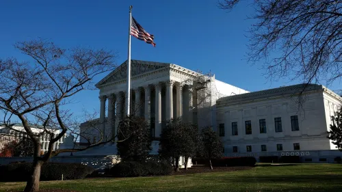 مبنى المحكمة العليا الأمريكية مع علم الولايات المتحدة يرفرف في المقدمة، يظهر في سماء زرقاء، مما يعكس أهمية القوانين والقرارات القضائية.