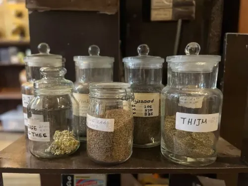 أوعية زجاجية تحتوي على أعشاب وتوابل مختلفة في متجر 't Zonnetje التاريخي بأمستردام، تعكس تراث القهوة والشاي العريق.
