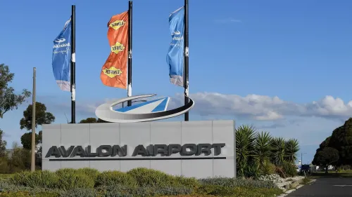 لافتة مطار أفالون في أستراليا، مع أعلام ملونة ترفرف في الهواء، تعكس حالة الطوارئ بعد حادثة تهديد مسلح.