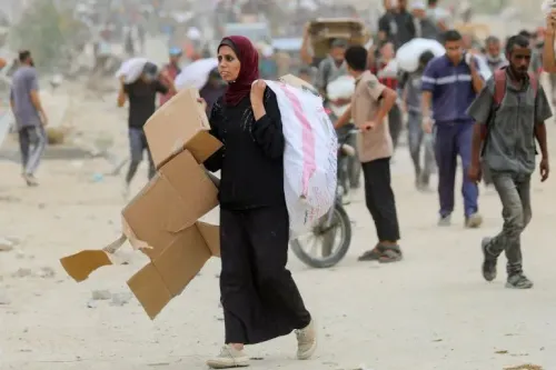 امرأة فلسطينية تحمل أكياس المساعدات الغذائية في غزة، وسط ازدحام من الناس الذين يسعون للحصول على الطعام في ظروف صعبة.