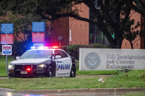 سيارة شرطة متوقفة أمام مبنى إدارة إنفاذ قوانين الهجرة والجمارك الأمريكية في دالاس، مع لافتات تحذيرية حول منطقة محظورة.