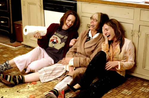 نساء يضحكن معًا في مطبخ، يجلسن على الأرض، مع فوضى حولهن، في مشهد يعكس روح المرح من فيلم "ذا فاميلي ستون".