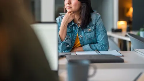 امرأة تفكر بعمق وهي تحمل قلمًا، محاطة بملاحظات ومشروبات، تعكس مشاعر القلق بشأن الاقتصاد والقرارات المالية.