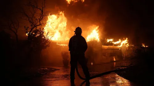 رجل إطفاء يقف أمام حريق كبير، محاط بألسنة اللهب والدخان، مما يبرز المخاطر التي يواجهها أثناء عمله في مكافحة الحرائق.