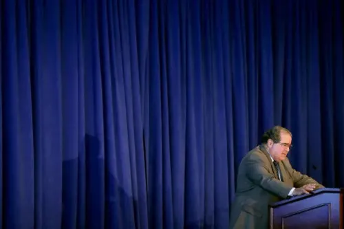 صورة لقاضي المحكمة العليا الراحل أنتونين سكاليا يتحدث أمام جمهور، مع ستارة زرقاء خلفه، تعكس أسلوبه الجريء في النقاشات القانونية.