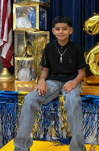 طفل يبلغ من العمر 11 عامًا يجلس مبتسمًا في حفل، محاط ببالونات وزينة، يمثل ضحية حادث مأساوي أثناء لعب مقلب مع ابن عمه.