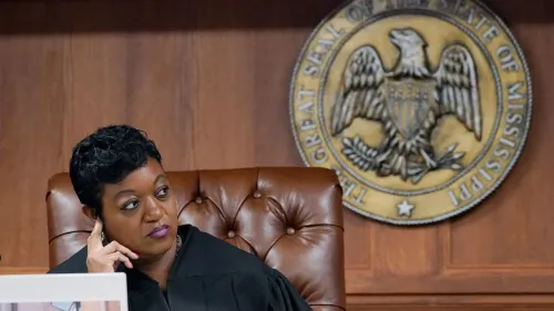 قاضية في ولاية ميسيسيبي أثناء جلسة استماع، خلفها شعار الولاية، تعكس القضايا القانونية المتعلقة بحرية الصحافة.