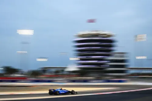 سيارة سباق فورمولا 1 زرقاء تتسابق على حلبة البحرين، مع خلفية مضاءة ومبنى مميز، تعكس حماس الموسم الجديد.