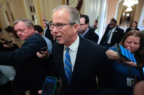 مجموعة من الأشخاص في مبنى حكومي، مع التركيز على رجل يرتدي بدلة وقميصًا أزرق، يتحدث مع الصحفيين حول تمويل وزارة الأمن الداخلي.